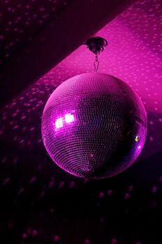 Disco ball in motion reflecting pink light in night club with copy-space