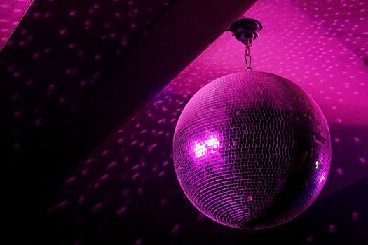 Disco ball in motion reflecting pink light in night club with copy-space