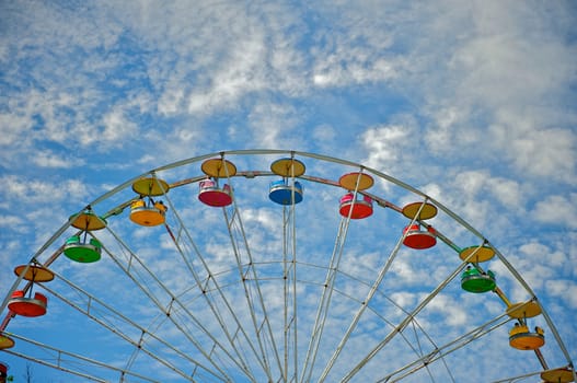 The baskets of a colorful ferris wheel at an amusement park surrounded by a gorgeous cloud-filled summer sky.
