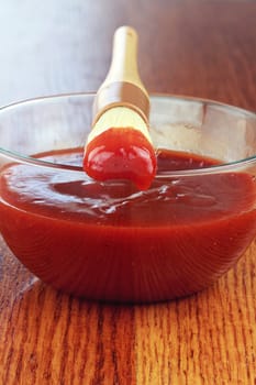 Basting brush and bowl of tangy barbecue sauce on an old battered wooden table with shallow depth of field.
