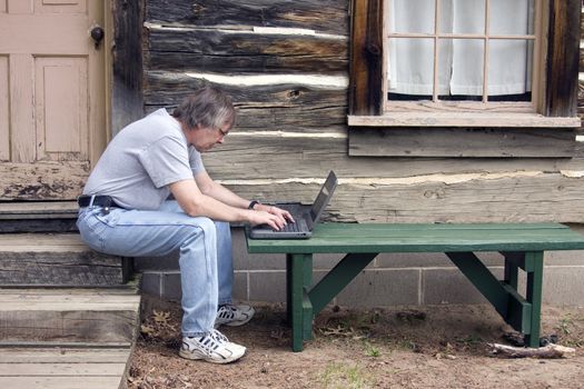 man working on his laptop computer in front of a log cabin