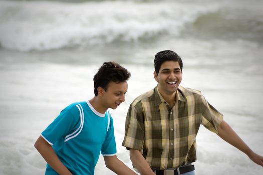 Two men standing on a beach at the shoreline, chatting and watching something