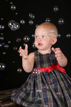 Cute blond toddler girl surrounded by bubbles sitting on a wooden trunk