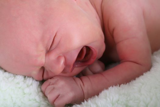 Caucasian new born baby girl crying on a green blanket