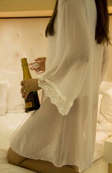 Woman holding a champagne bottle on a bed 