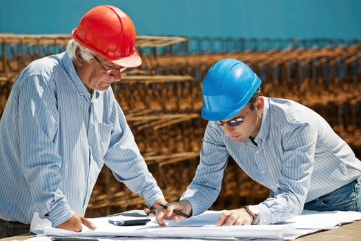 Young engineer shows a senior foreman the next steps in a construction project. Authentic professionals and site