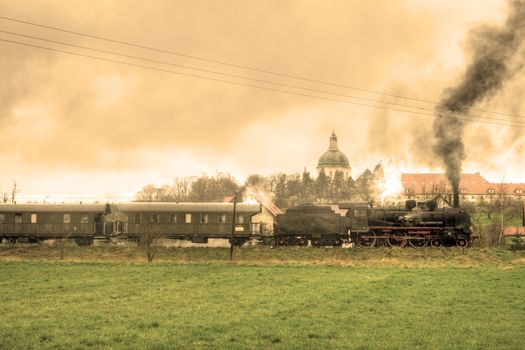 Old retro steam train passing the fields with a palace in background
