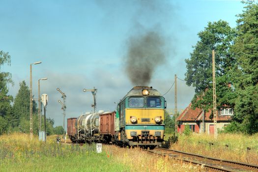 Rural summer landscape with freight train starting from the station
