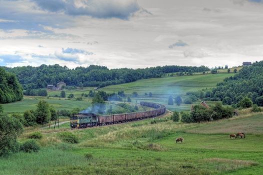 Freight train hauled by diesel locomotive passing the hilly landscape
