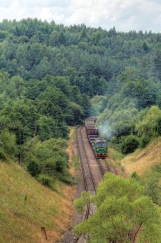 Freight train hauled by diesel locomotive passing the hilly forest
