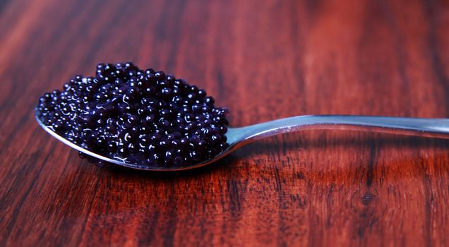 Black caviar on a spoon against a mahoney table