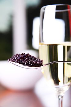 Black caviar on a spoon next to a glass of champagne