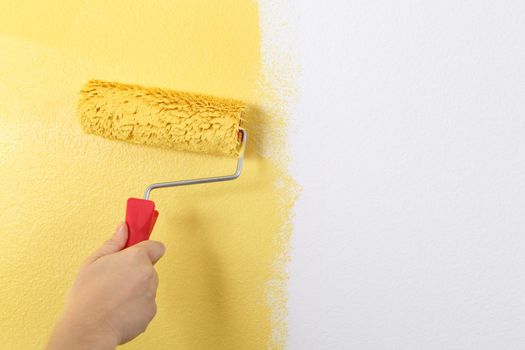 Photo of painting a wall with a roller and yellow paint.