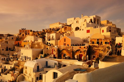 Image shows the traditional village of Oia, on the Greek island of Santorini with hundreds of tourists waiting for one of its famous sunsets