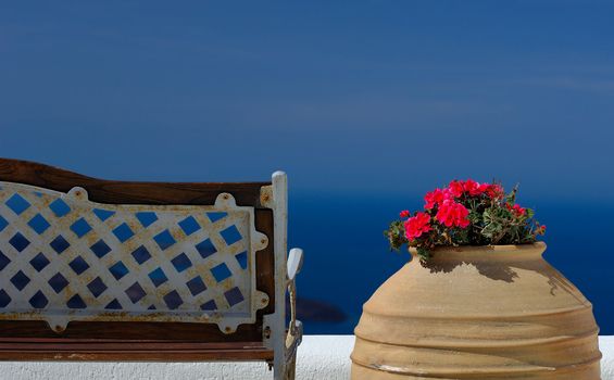 Image shows a bench and a pot with flowers on the island of Santorini overlooking the magnificent view