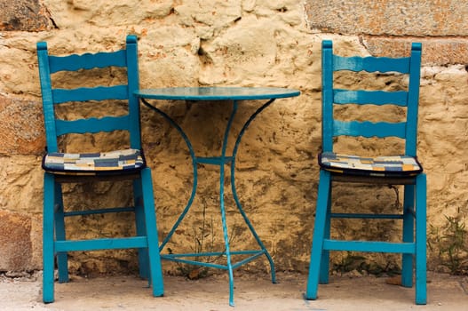 Blue table and chairs in a country coffee shop, against a highly textured wall. Image captured in southern Greece.