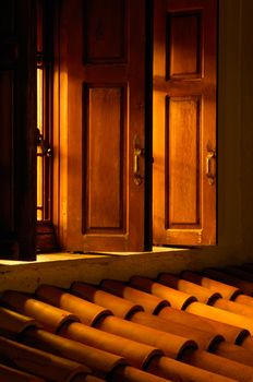 Picture shows an open window allowing golden light to illuminate the roof outside 