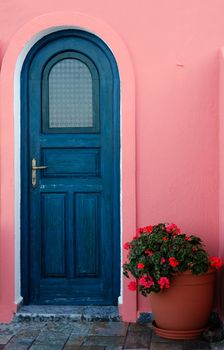 Image shows a blue door with a flower pot next to it, captured on a Greek island.  