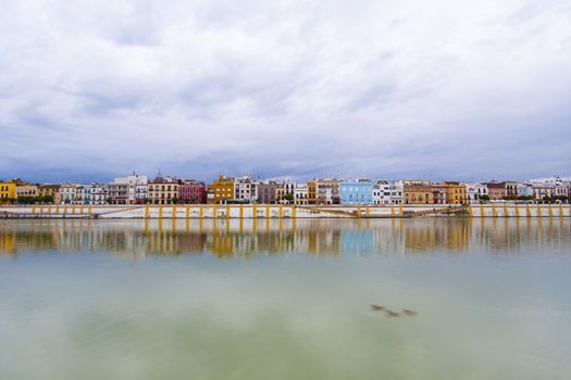 Colorful panorama of Seville riverside on the overcast day, forming amazing pastel colors and reflections in the river.
