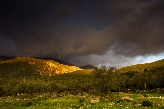 Greek landscape right after a storm with emerging rays of sun lighting the tip of the mountain