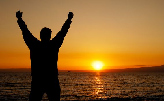 Silhouette of a man facing a glorious sunset, with his hands in the air