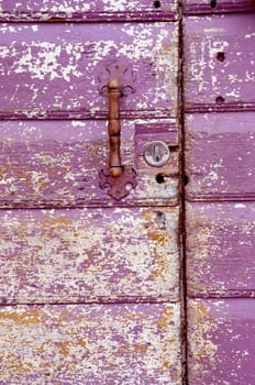 Background of an old painted, crumbled door. Handle on purple wooden planks.