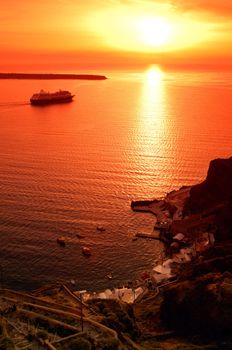 Image shows one of the famous sunsets in Santorini, greece, while a cruise ship is travelling towards the open sea
