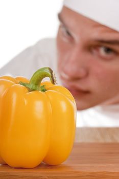 The young chef in chef's hat is considering a pepper.