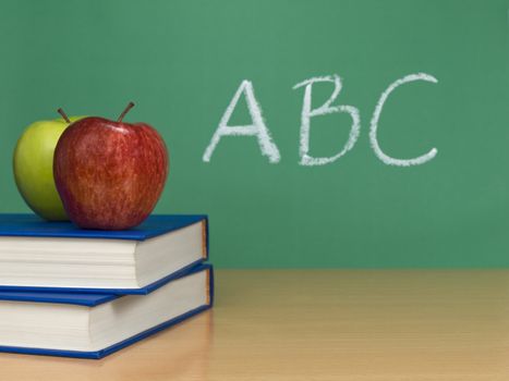 ABC written on a chalkboard. Two apples over books on the foreground.