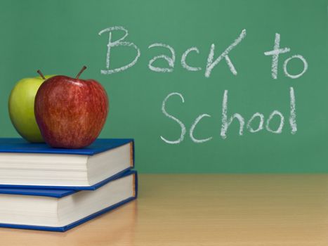 Back to school written on a chalkboard. Two apples over books on the foreground.