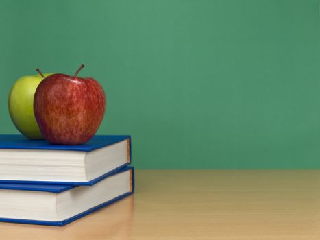 A blank chalkboard with two apples over books.