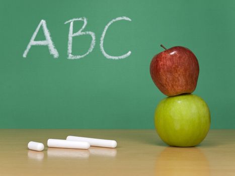 ABC written on a chalkboard. Some chalks and a red apple over a green one on the foreground.