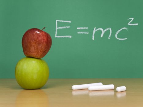 Einsteins formula of theory of relativity on a chalkboard. Some chalks and apples on the foreground.