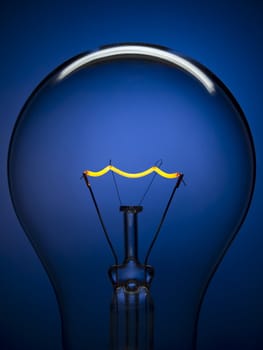 Close up on a transparent light bulb over a blue background. Tungsten glowing filament.