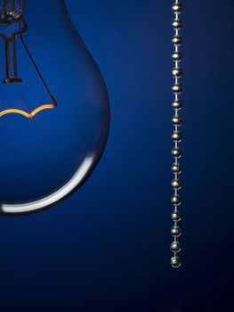 Close up on a transparent light bulb with a pull switch over a blue background.