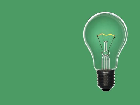 A transparent light bulb over a green background. Tungsten glowing filament. Copy space.