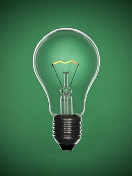 A transparent light bulb over a green background. Tungsten glowing filament.