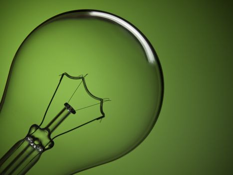 Close up on a transparent light bulb over a green background.