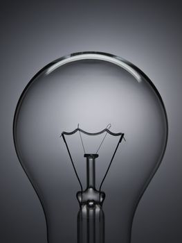 Close up on a transparent light bulb over a grey background.