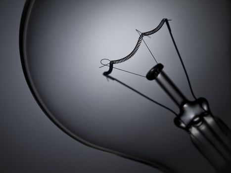 Close up on a transparent light bulb over a grey background.