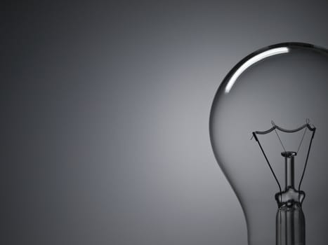 Close up on a transparent light bulb over a grey background. Copy space.