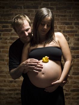 A yellow rubber duck is sitting over the big round belly. The pregnant couple patiently waits.