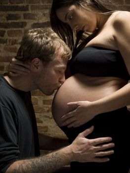 A young man kisses his pregnant woman.