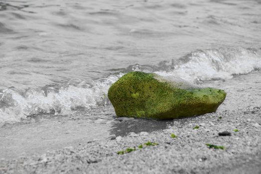 Green stone on the beach. The beach is black and white. The stone is green in its natural color.