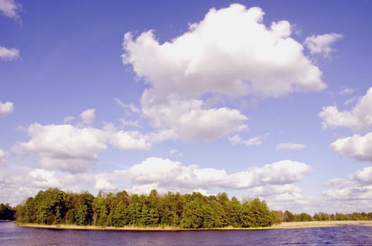 Small lake island surrounded by water and cumulus clouds over it.