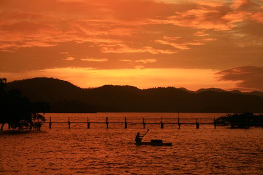 orange sunset with silhouettes of mountain, bridge and boat 
