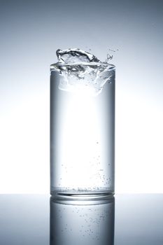 Glass filled with water with splash on a reflecting surface
