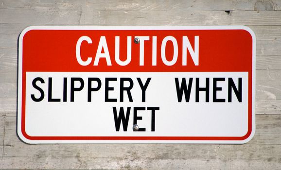 Caution Slippery When Wet Sign is a capture of a Red and White Warning Sign on a weathered wood board background with a knot.
