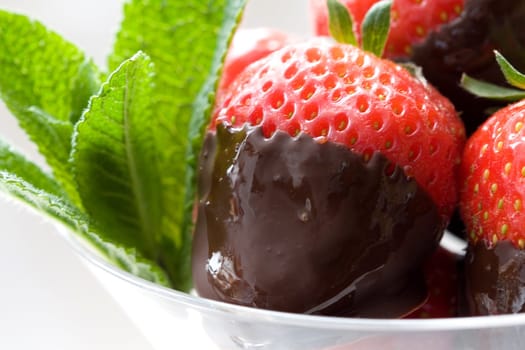 Strawberries with their tips dipped in hot chocolate served in a glass with mint leaves