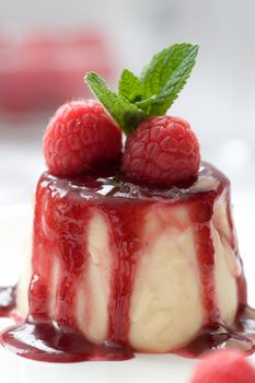 Small panna cotta covered with strawberry sauce and decorated with fresh raspberries and a mint leave